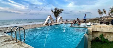 Una piscina con vista al océano, una palmera y una persona caminando.
