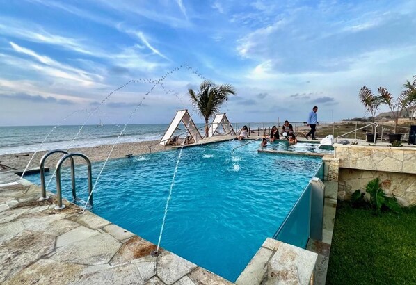 A swimming pool with a view of the ocean, a palm tree, and a person walking.