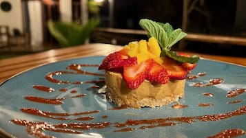 Postre en un plato con borde azul, adornado con fresas, mango y hojas de menta.