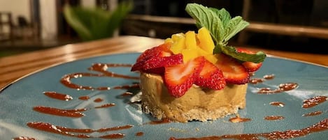 Postre en un plato con borde azul, adornado con fresas, mango y hojas de menta.