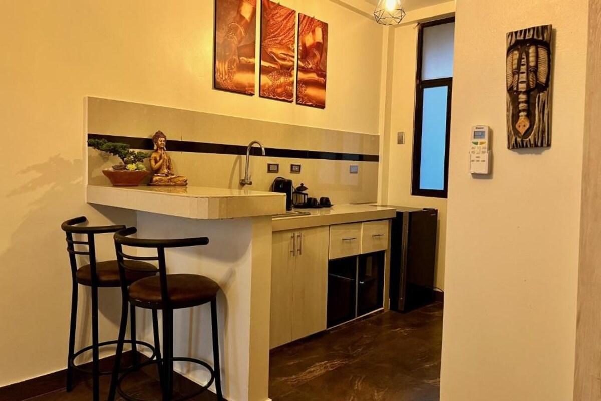 A compact kitchen with a bar stool, a Buddha statue, and artwork on the wall.