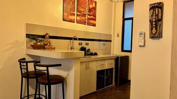 Una cocina compacta con un taburete de bar, una estatua de Buda y obras de arte en la pared.