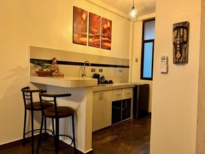 A compact kitchen with a bar stool, a Buddha statue, and artwork on the wall.
