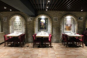 A restaurant with brick walls, arched windows, and red chairs. Tables are set with white tablecloths. - Reikartz Astana (Astana)