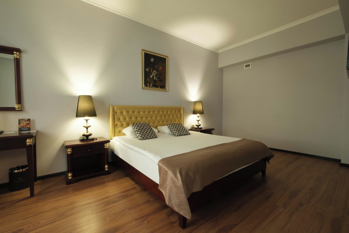 A neatly arranged hotel room with a large bed, two bedside tables with lamps, a wooden headboard, and a framed picture on the wall.