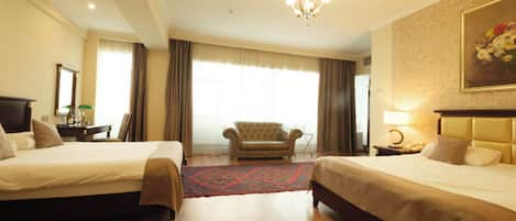 A hotel room with two beds, a chandelier, a large window with curtains, a sofa, and a painting on the wall.