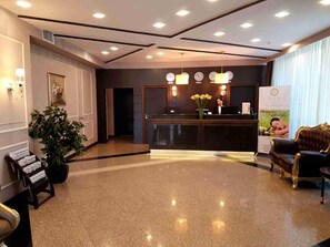A hotel reception area with a reception desk, a potted plant, a sofa, and a wall-mounted clock. - Reikartz Astana (Astana)