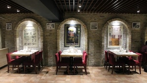 A restaurant with brick walls, arched windows, and red chairs. Tables are set with white tablecloths.