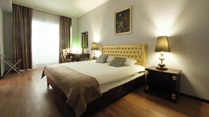 A hotel room with a large bed, two bedside lamps, a painting on the wall, and a desk with a chair.