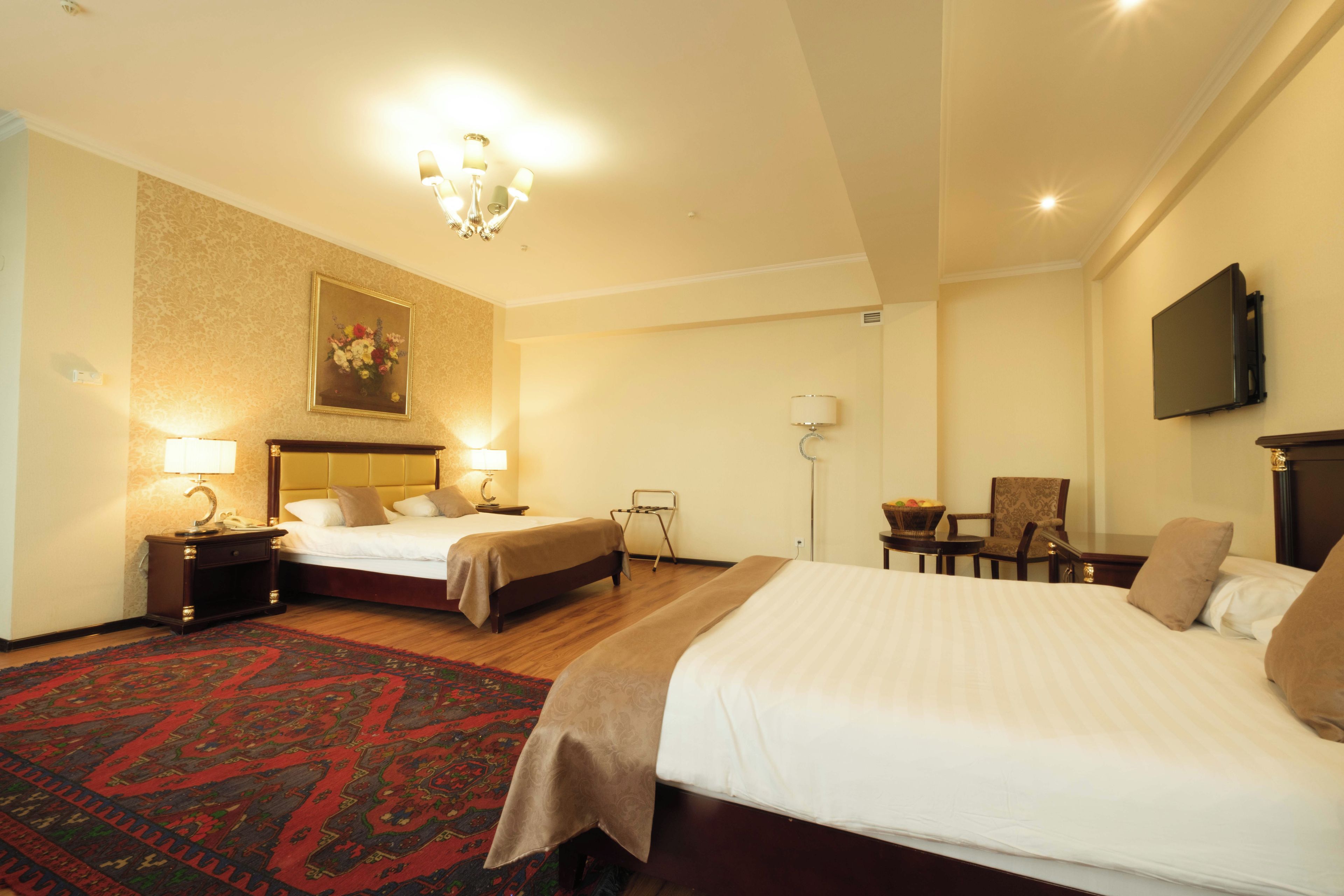 A hotel room with two beds, a chandelier, a television, and a red patterned rug.