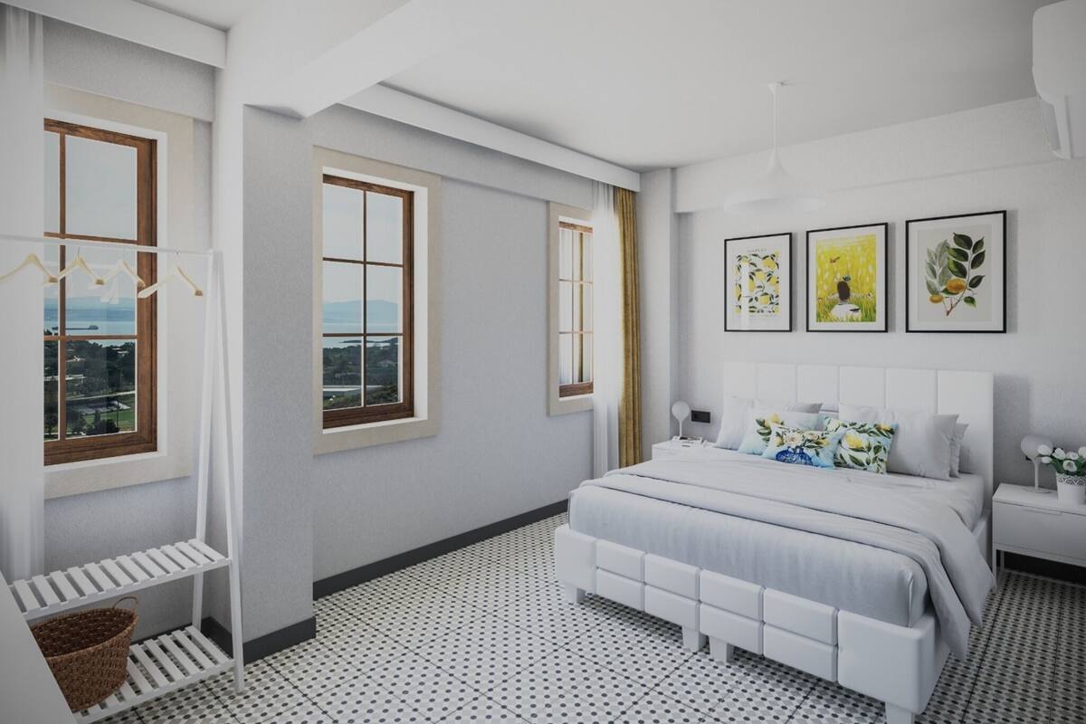 Ein modernes Schlafzimmer mit einem großen Bett, zwei Fenstern, Blick auf die Stadt und Kunstwerken an der Wand.
