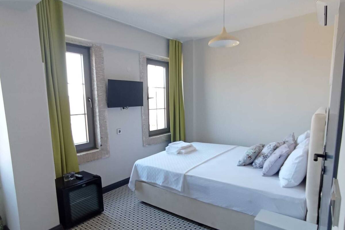 Ein Schlafzimmer mit Bett, Fernseher, kleinem Schreibtisch und einem Fenster mit Vorhängen.