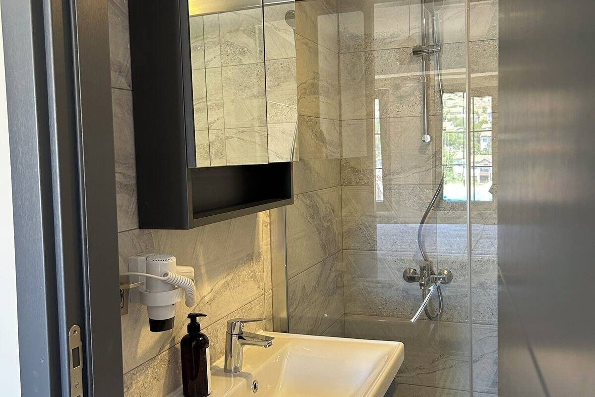 Ein modernes Badezimmer mit einer gläsernen Dusche, einem weißen Waschbecken und einem Spiegel darüber.