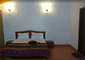 A room with a bed, two wall-mounted lights, a nightstand, and a door. - Nikhara Garden And Resorts (Mandya)