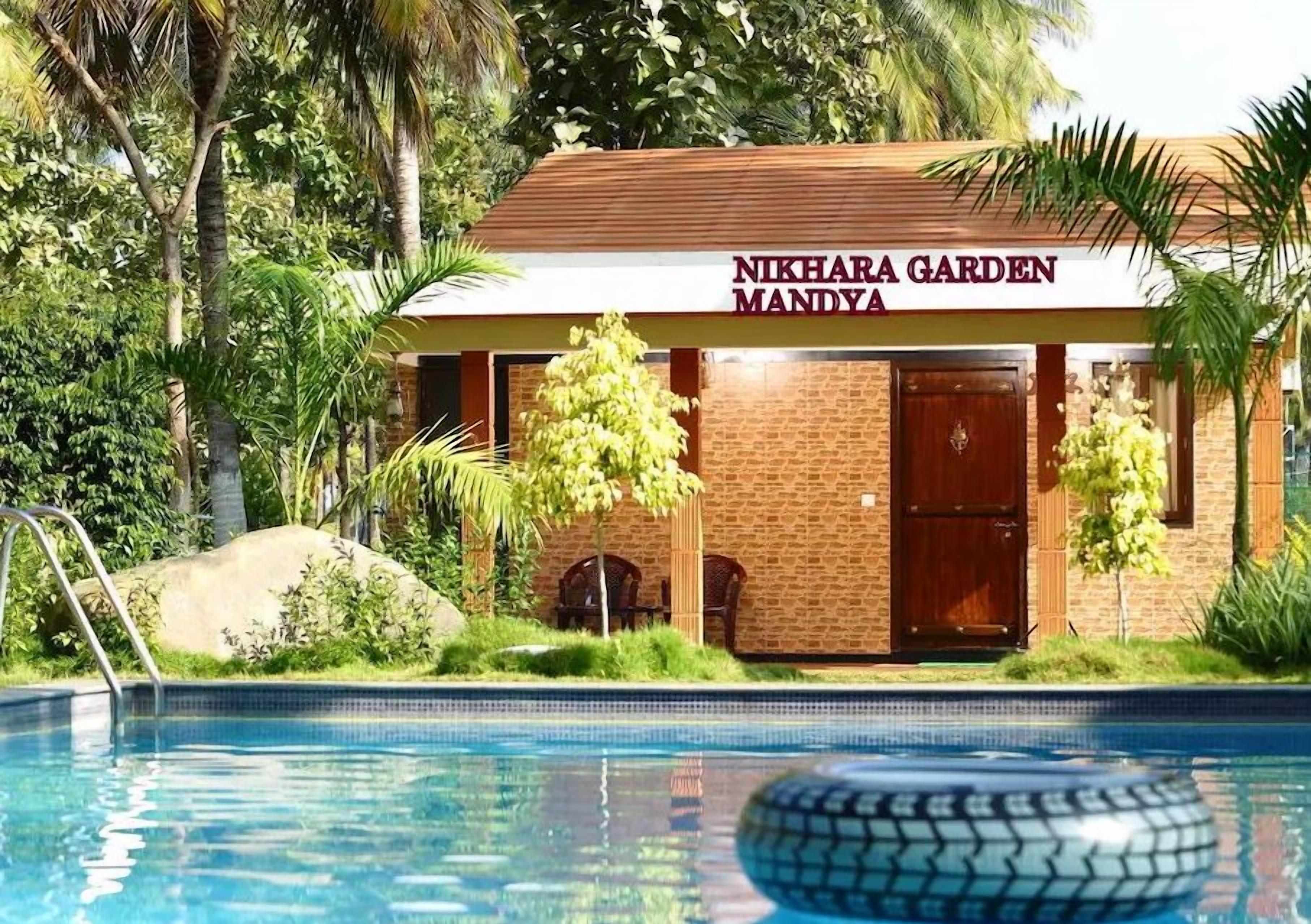 Un edificio con la leyenda 'NIKHARA GARDEN MANDYA' y una piscina al frente.
