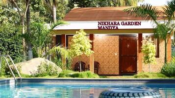 Un edificio con la leyenda 'NIKHARA GARDEN MANDYA' y una piscina al frente.