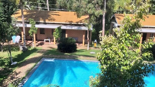 Une piscine entourée de verdure et un bâtiment doté d’un toit en tuiles.