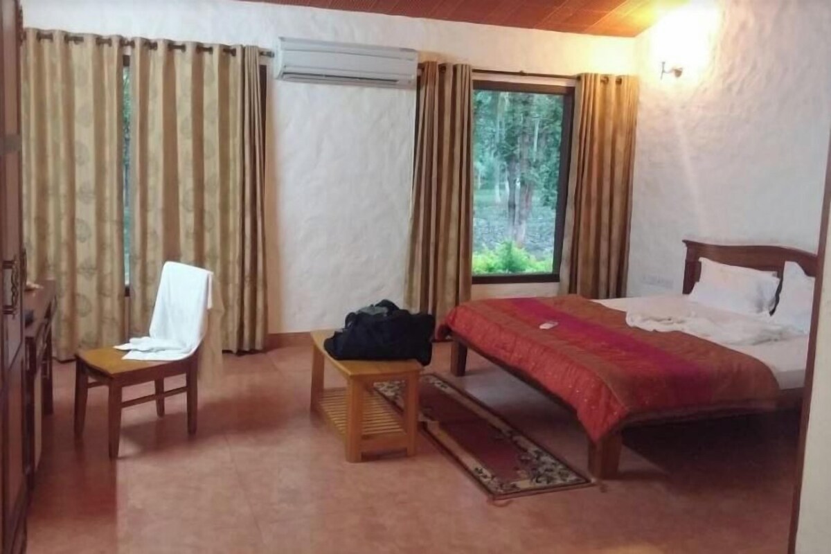 A hotel room with a bed, a chair, a small table, and a window with curtains.