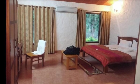 Een hotelkamer met een bed, een stoel, een klein tafeltje en een raam met gordijnen.