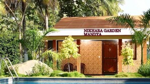 Un bâtiment portant l’inscription « Nikhara Garden Mandya », avec une piscine au premier plan.