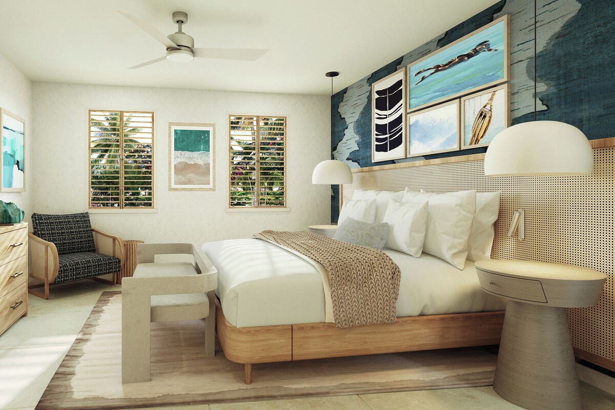 A bedroom with a bed, a TV, a desk, a chair, and artwork on the walls.