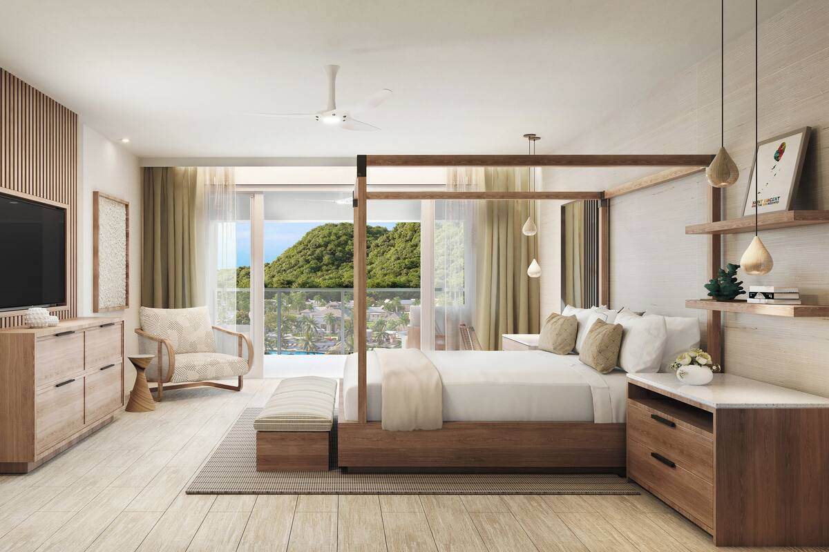 Quarto moderno com uma cama grande, televisão, poltrona e vista para uma paisagem verde.