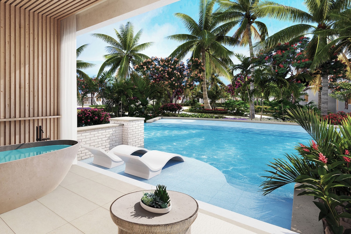 A modern pool area with a large bathtub, lounge chairs, and tropical plants.