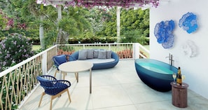 A balcony with a sofa, chairs, a table, and a decorative bowl with glasses and a bottle.