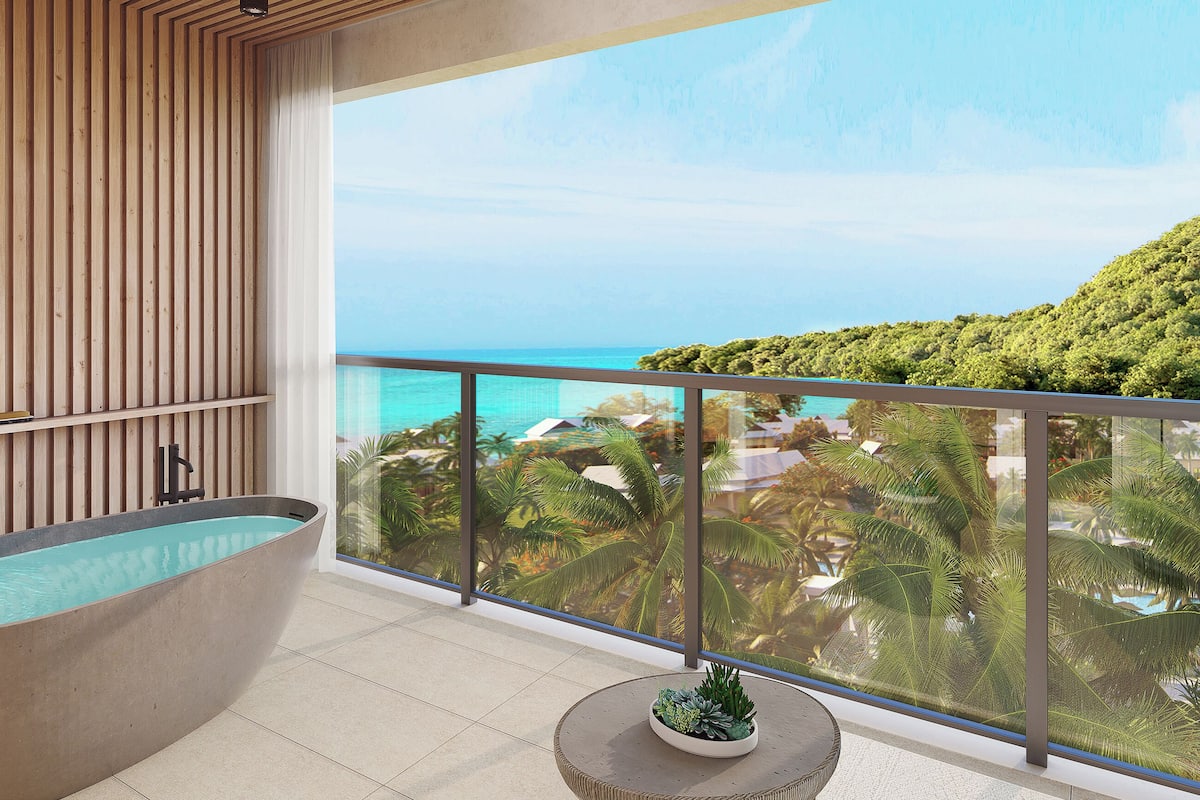A modern bathroom with a freestanding bathtub, a small potted plant, and a balcony with a view of the ocean and greenery.