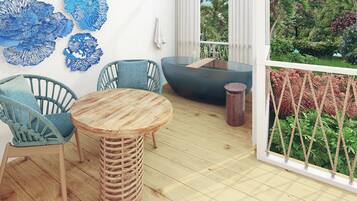 A wooden deck with a round table and two wicker chairs, a blue sofa, and a view of a lush garden through large windows.