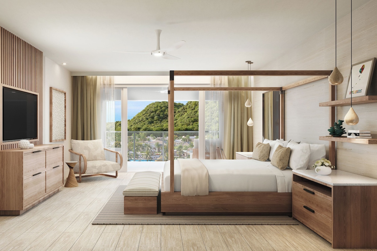 A modern bedroom with a large bed, a TV, a chair, and a view of a green landscape.
