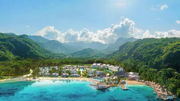 Un resort con varias construcciones, una playa y una vista despejada de las montañas circundantes.