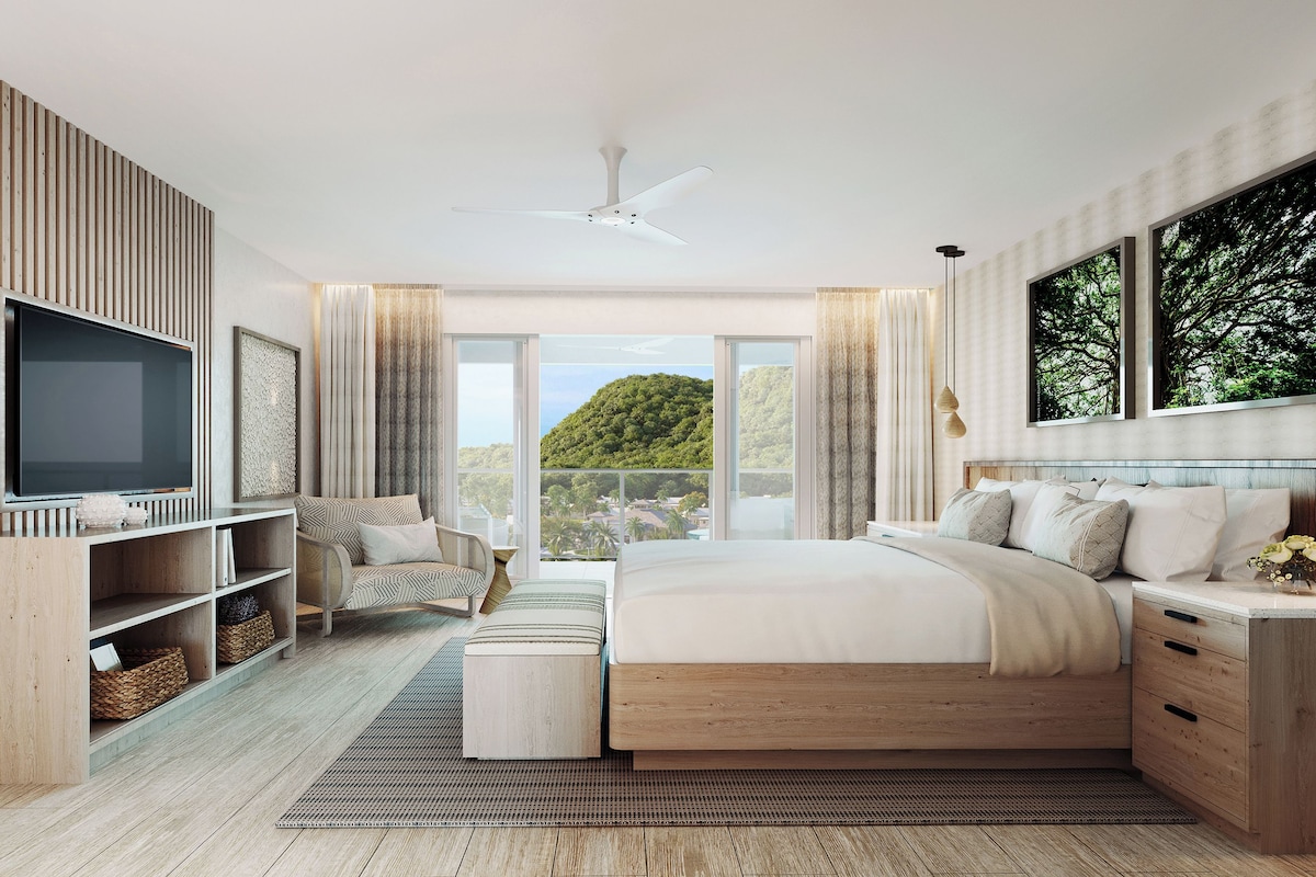 A modern bedroom with a large bed, a TV, wooden shelving, and a view of greenery.