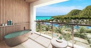 A modern bathroom with a freestanding bathtub, a small round table with a plant, and a balcony with a view of a pool and tropical landscape.