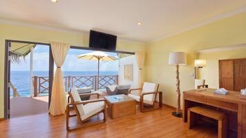 A spacious room with wooden flooring, a large window with a view of the sea, a wooden desk, a chair, a sofa, and a lamp.