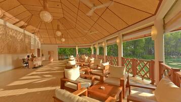 A covered outdoor seating area with wooden furniture and a view of greenery.