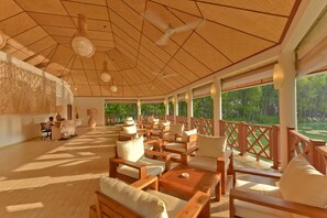 A covered outdoor seating area with wooden furniture and a view of greenery.