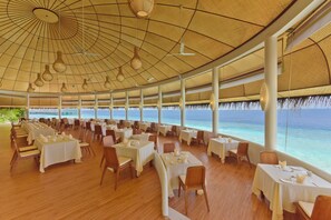 Un espaiós restaurant amb taules preparades per dinar, grans finestres que ofereixen vistes a l'oceà i un sostre amb lluminàries penjants.