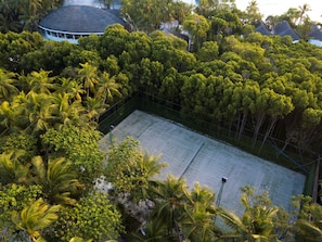 An aerial view of a tennis court surrounded by dense tropical foliage, with a dome-roofed building in the background. - Dreamland Maldives (Hirundhoo)