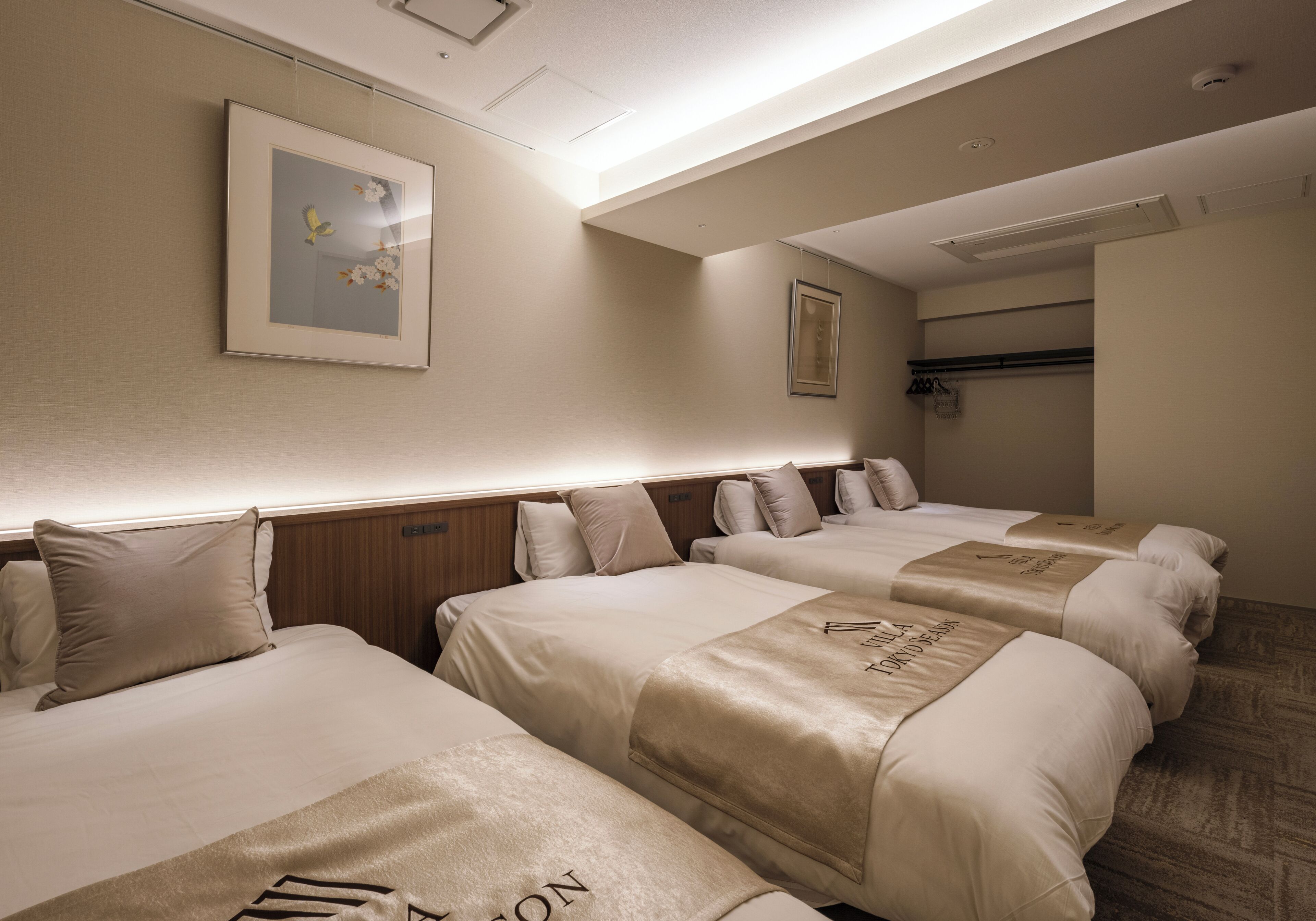 A hotel room with four beds arranged in a row, a framed picture on the wall, and a ceiling light fixture.
