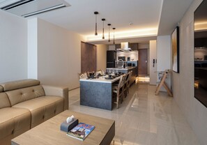 Una sala de estar moderna con un sofá, una mesa de centro con una revista, una cocina con una isla central y un comedor con sillas.