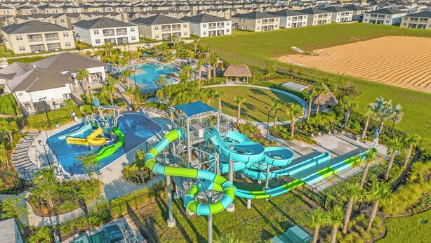 An aerial view of a resort with a large pool area, water slides, and a well-maintained lawn. - Champions Gate Resort Homes (Davenport)