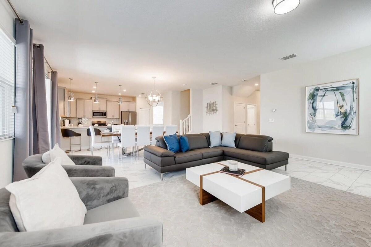 Ein modernes Wohnzimmer mit einem Ecksofa, einem weißen Couchtisch und einem Essbereich im Hintergrund.