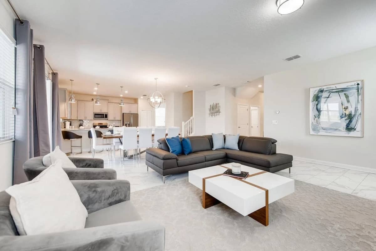A modern living room with a sectional sofa, a white coffee table, and a dining area in the background.