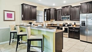 A modern kitchen with dark cabinets, stainless steel appliances, and a central island with bar stools. - Champions Gate Resort Homes (Davenport)