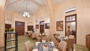 A spacious dining area with high ceilings, arched doorways, and a chandelier. Tables are set with white tablecloths and chairs. - Arova Woods Zinc Journey (Mawal)