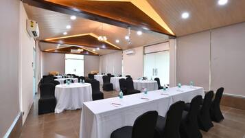 A conference room with round tables, black chairs, white tablecloths, and ceiling lights.