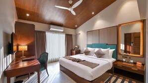 A hotel room with a bed, desk, chair, and a ceiling fan. - Arova Woods Zinc Journey (Mawal)