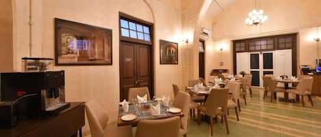 A dining area with tables set for guests, a coffee machine, and framed artwork on the walls.