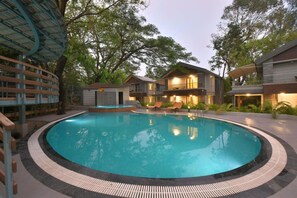 A pool area with a circular pool, wooden deck, and a building with multiple balconies. - Arova Woods Zinc Journey (Mawal)